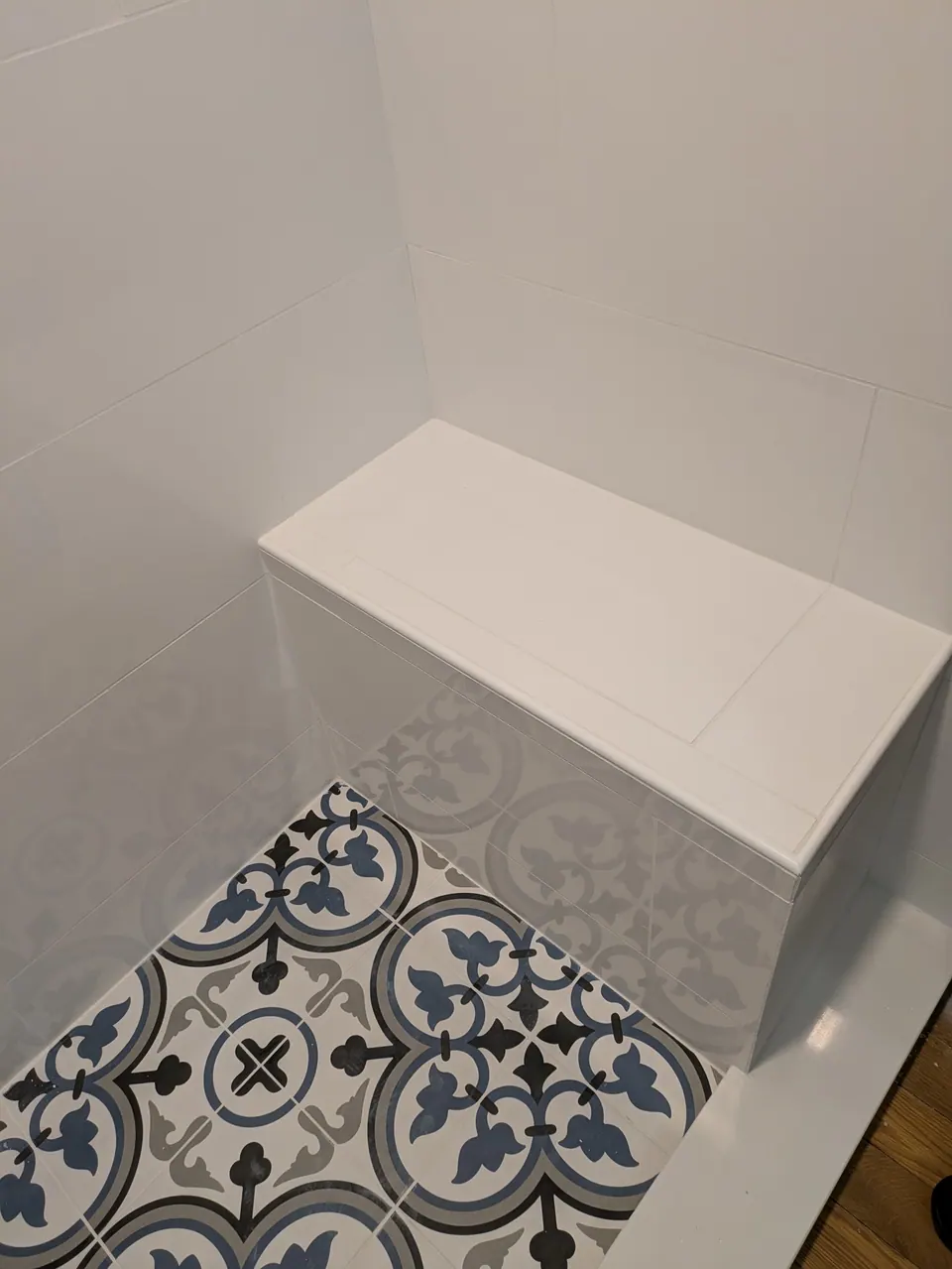 Built-in white tiled shower bench above blue and gray patterned floor tile.