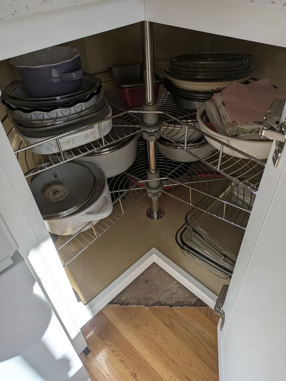 Corner base cabinet open, showing a two-tier wire lazy Susan loaded with baking dishes and pots.