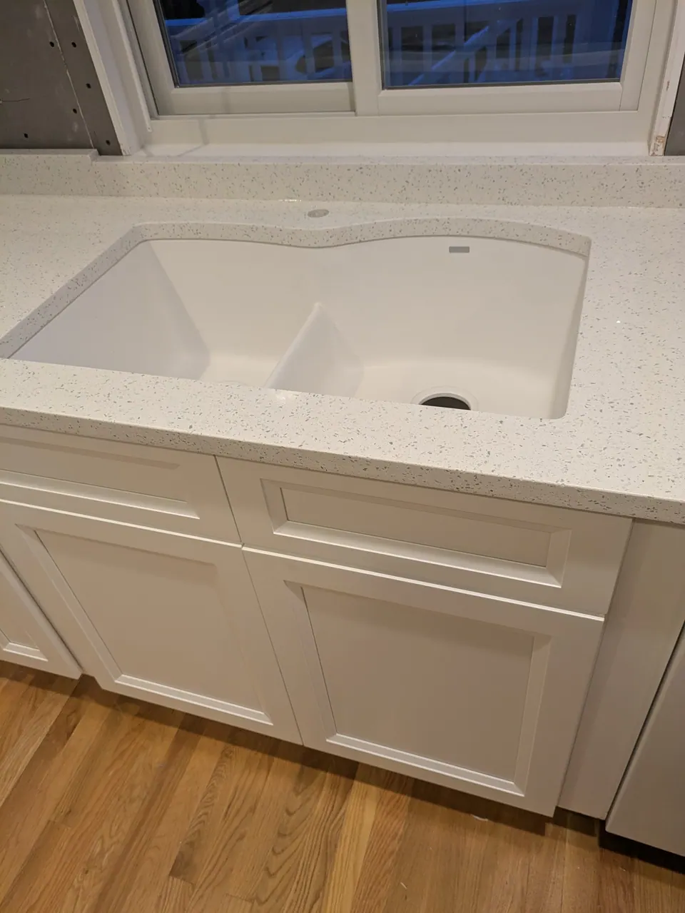 In progress: white undermount double-bowl sink in the speckled countertop over a white sink base, no faucet yet.