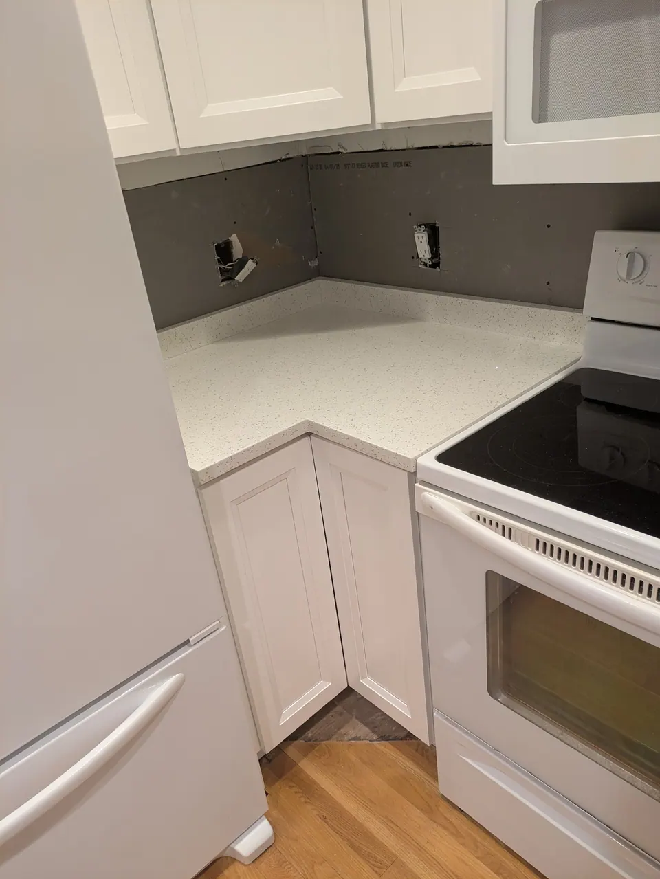 In progress: corner countertop and white corner base cabinet beside the range, bare wall with open outlets.