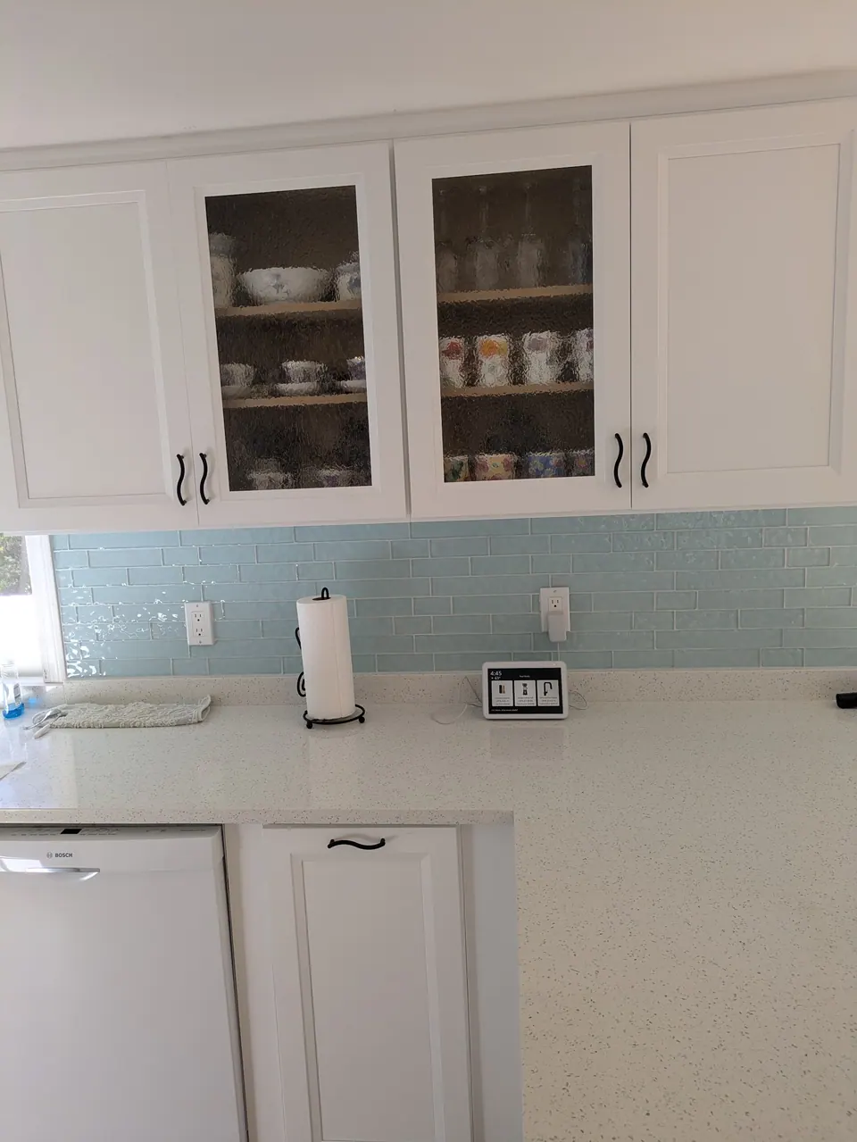 White wall cabinets with two textured glass doors above a speckled white countertop and light blue backsplash.