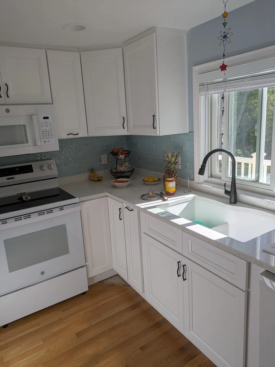 White shaker cabinets with black pulls, light blue tile backsplash, white range and sink under a window.