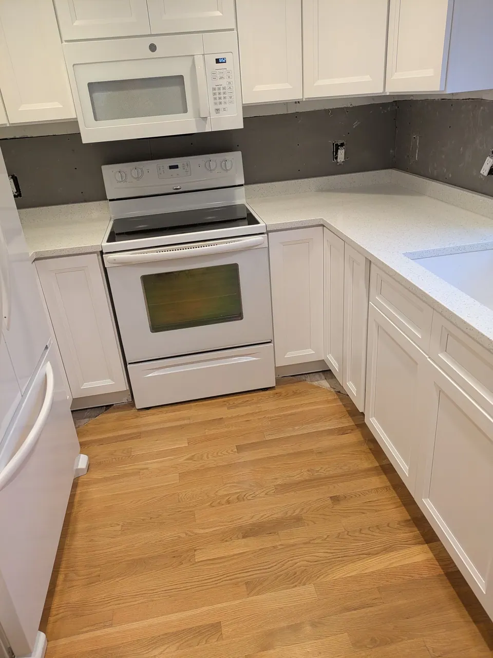 In progress: white cabinets around the range and microwave, countertop in, wall still bare of backsplash.