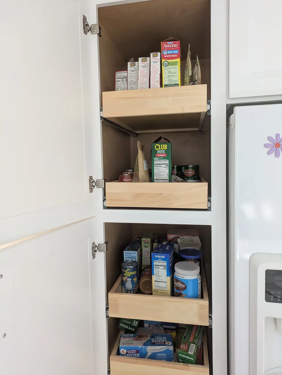 Upper and lower pantry sections open, each with wood roll-out trays holding boxed and canned food.