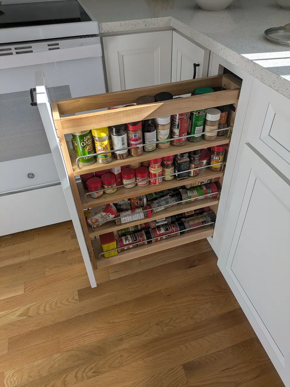 Pull-out spice rack beside the range, four shelves of spice jars in a white base cabinet.
