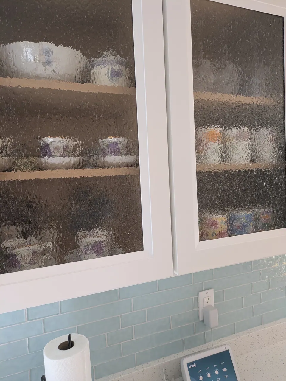 Close-up of textured glass cabinet doors with dishes behind, above light blue subway tile.