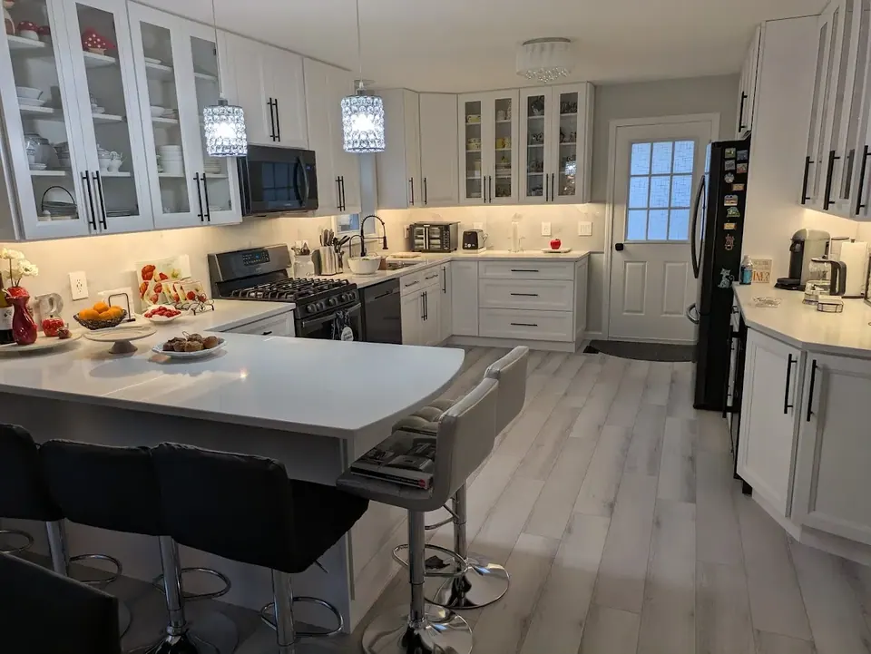 White shaker kitchen with glass-front wall cabinets, a peninsula with bar stools and light gray wood-look floor.