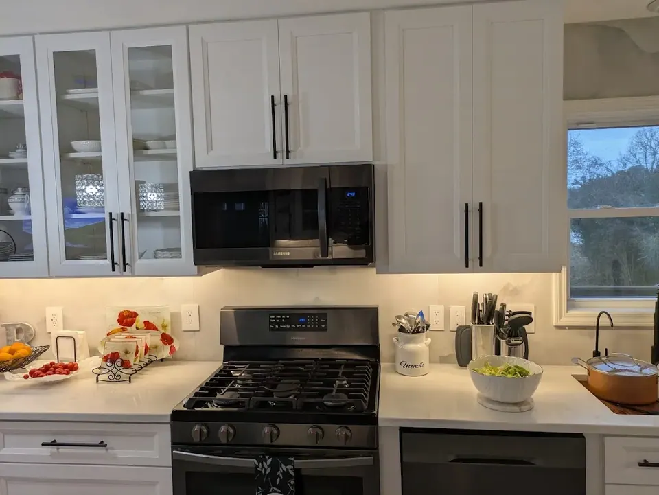 White wall cabinets and an over-the-range microwave above a gas range, with under-cabinet lighting on.