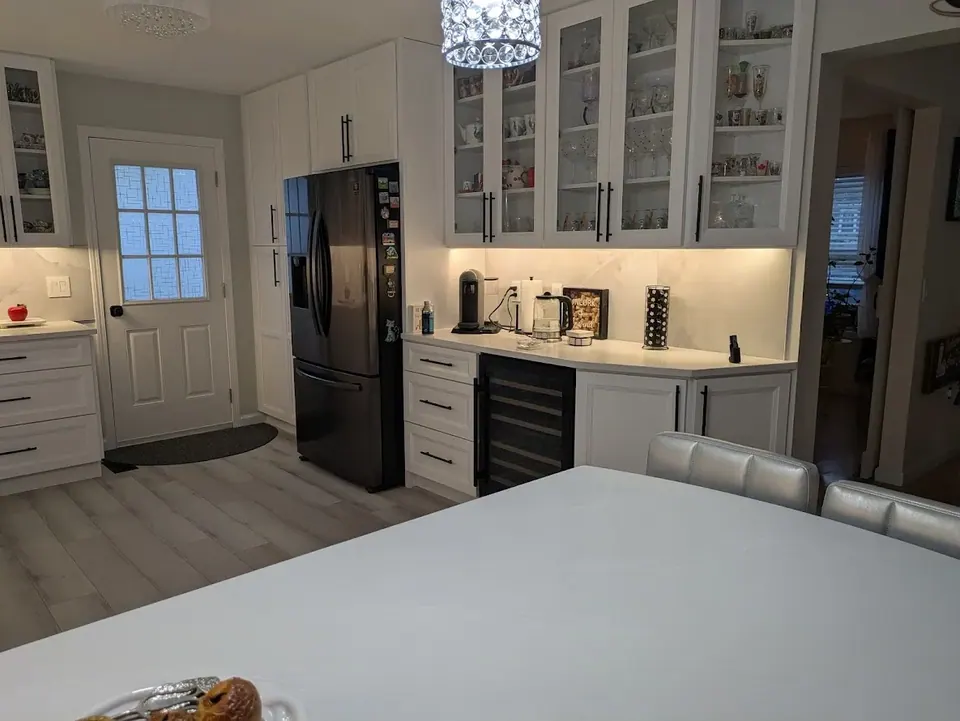 White pantry cabinets around a dark refrigerator and a beverage counter, seen across the white peninsula.