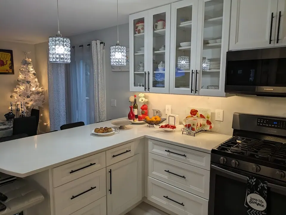 White peninsula with drawer bases, glass-front wall cabinets and two pendant lights beside the gas range.