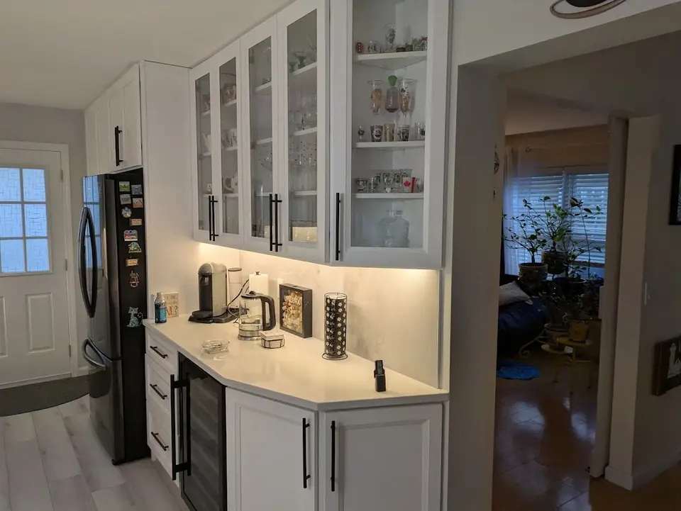 Beverage counter with glass-front wall cabinets, an under-counter wine cooler and an angled end cabinet by the doorway.