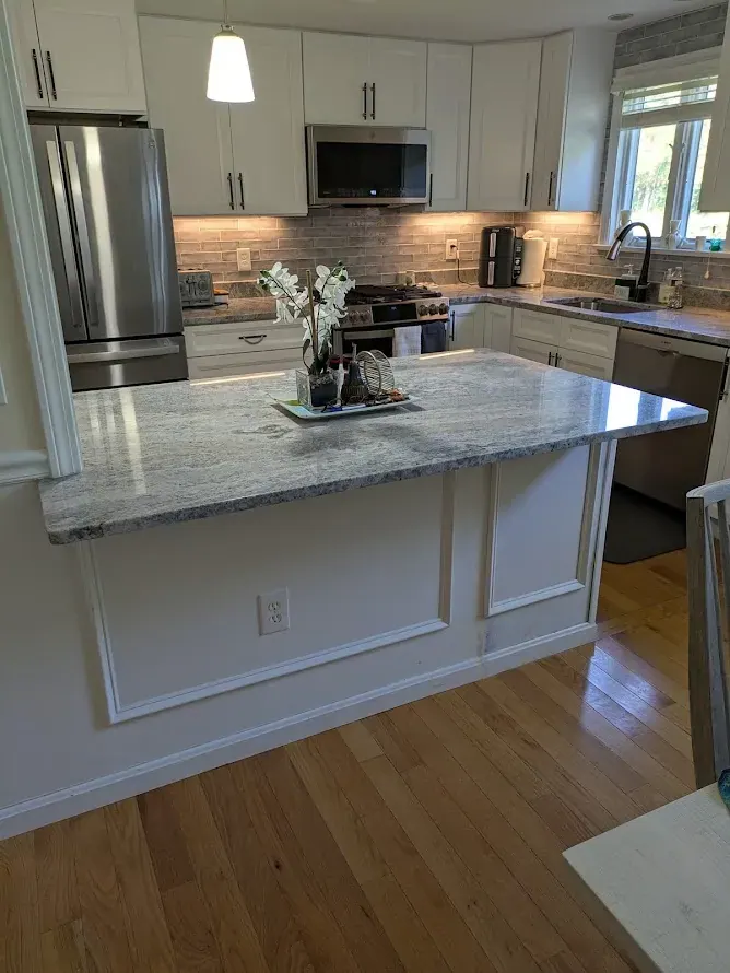 White shaker kitchen seen over a peninsula with light gray countertop and paneled back.