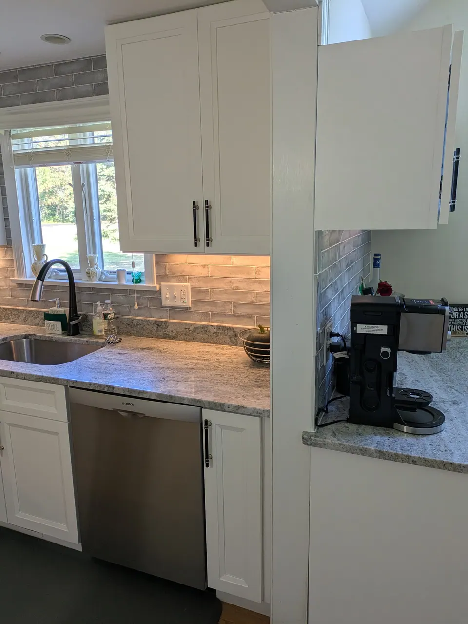 White wall cabinet above the dishwasher beside the sink window, bar counter at right.