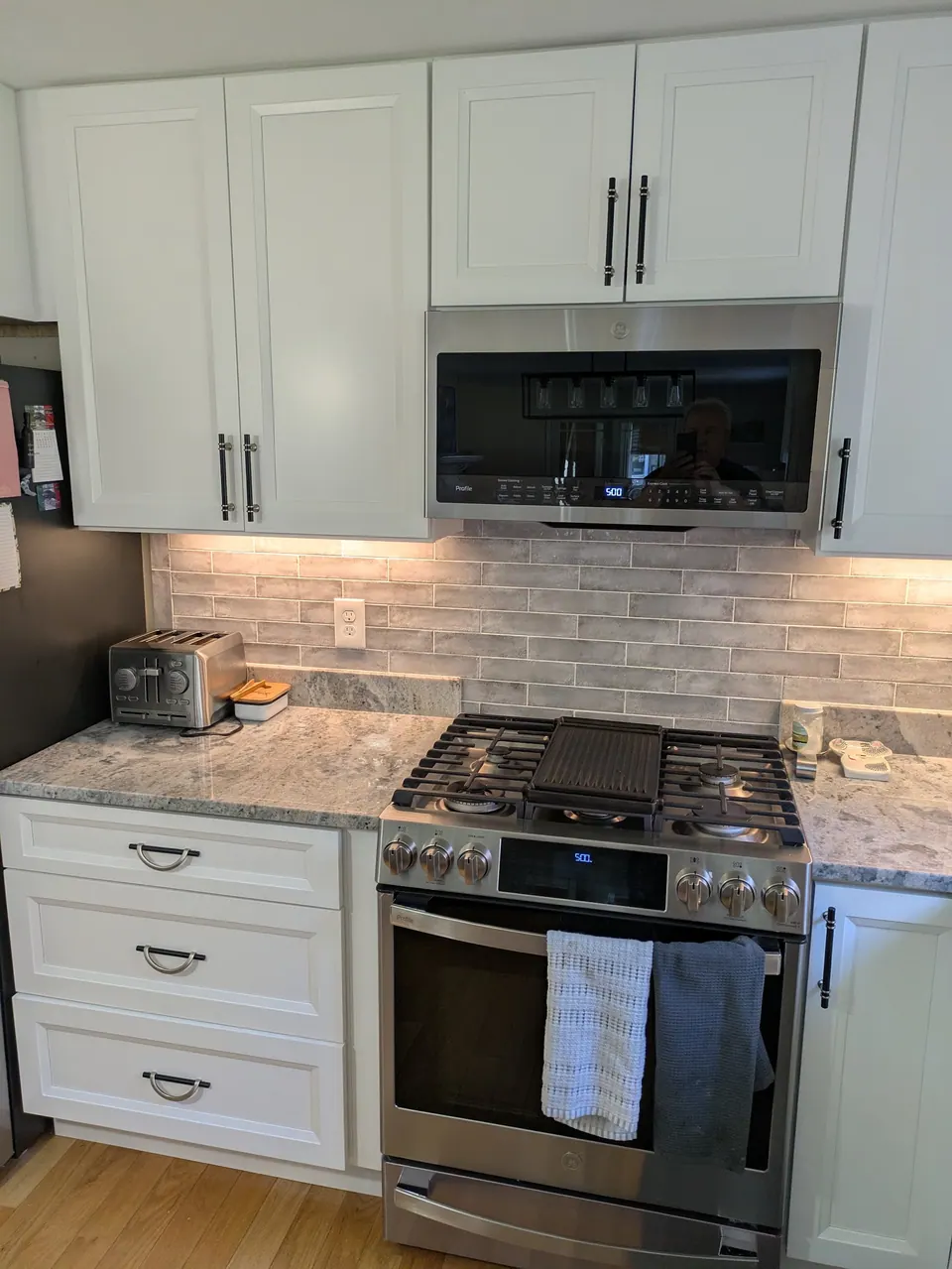 White wall cabinets and microwave above a gas range, three-drawer base at left.