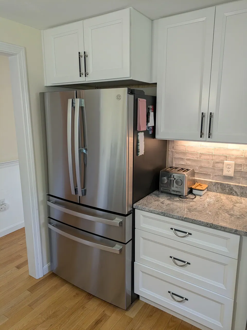 Stainless refrigerator with a white cabinet above, wall cabinet and drawer base beside it.
