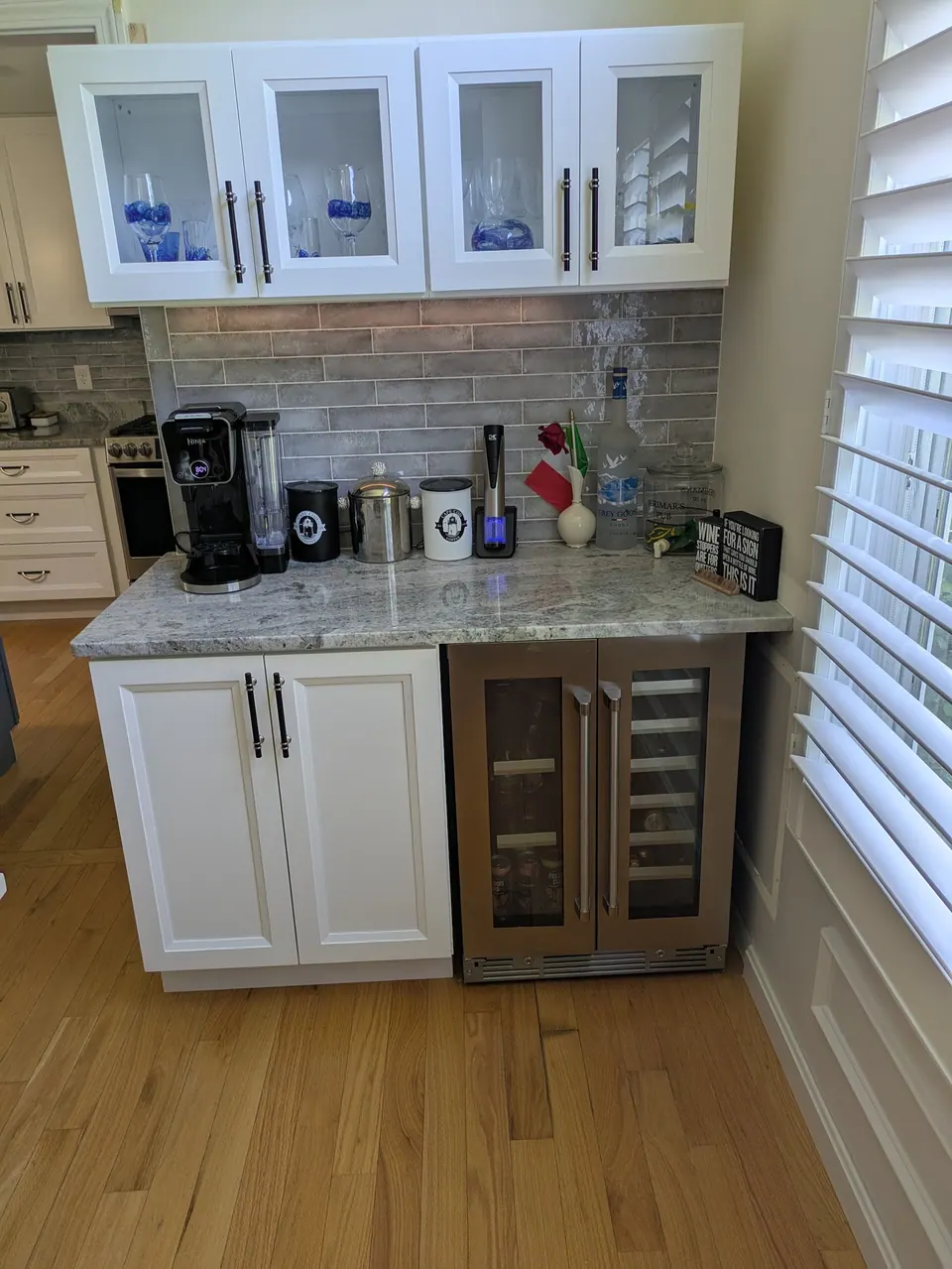 White glass-front wall cabinets above a countertop, base cabinet and under-counter beverage cooler.