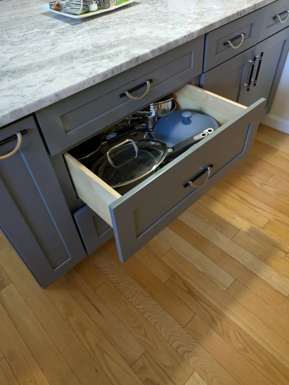 Gray peninsula drawer open with pots and lids under a light gray countertop.