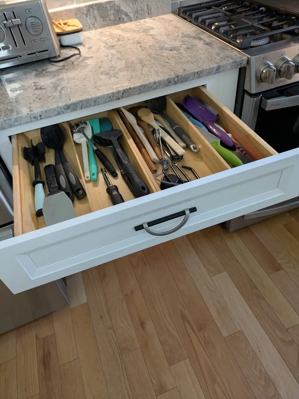 White top drawer open with a divider organizer holding cooking utensils, beside the range.