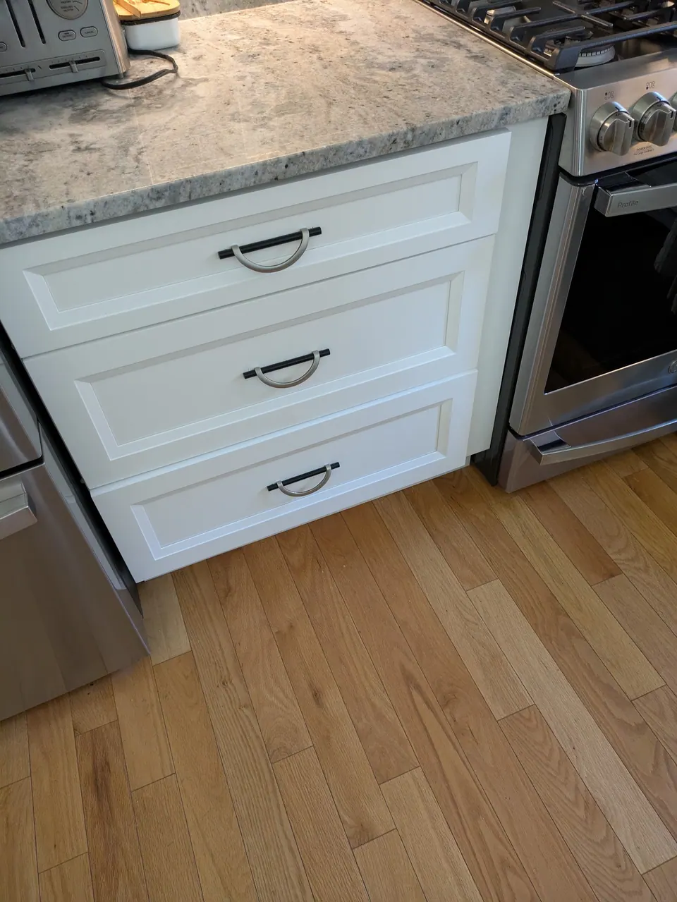 White three-drawer base with black and brushed arched pulls beside the range.