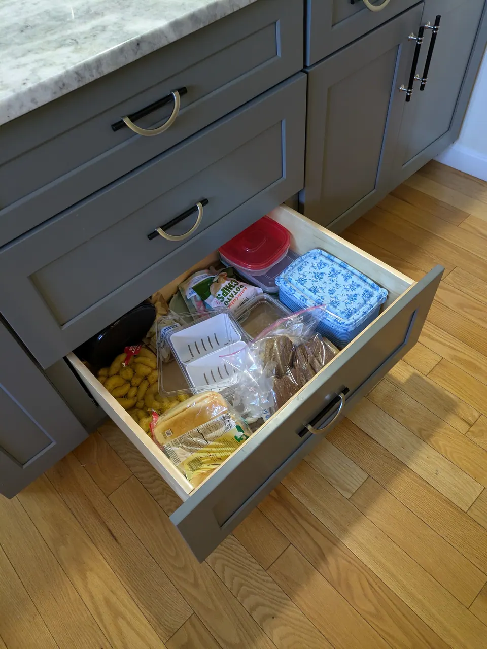 Gray bottom drawer open with bread and food containers, gray doors beside it.