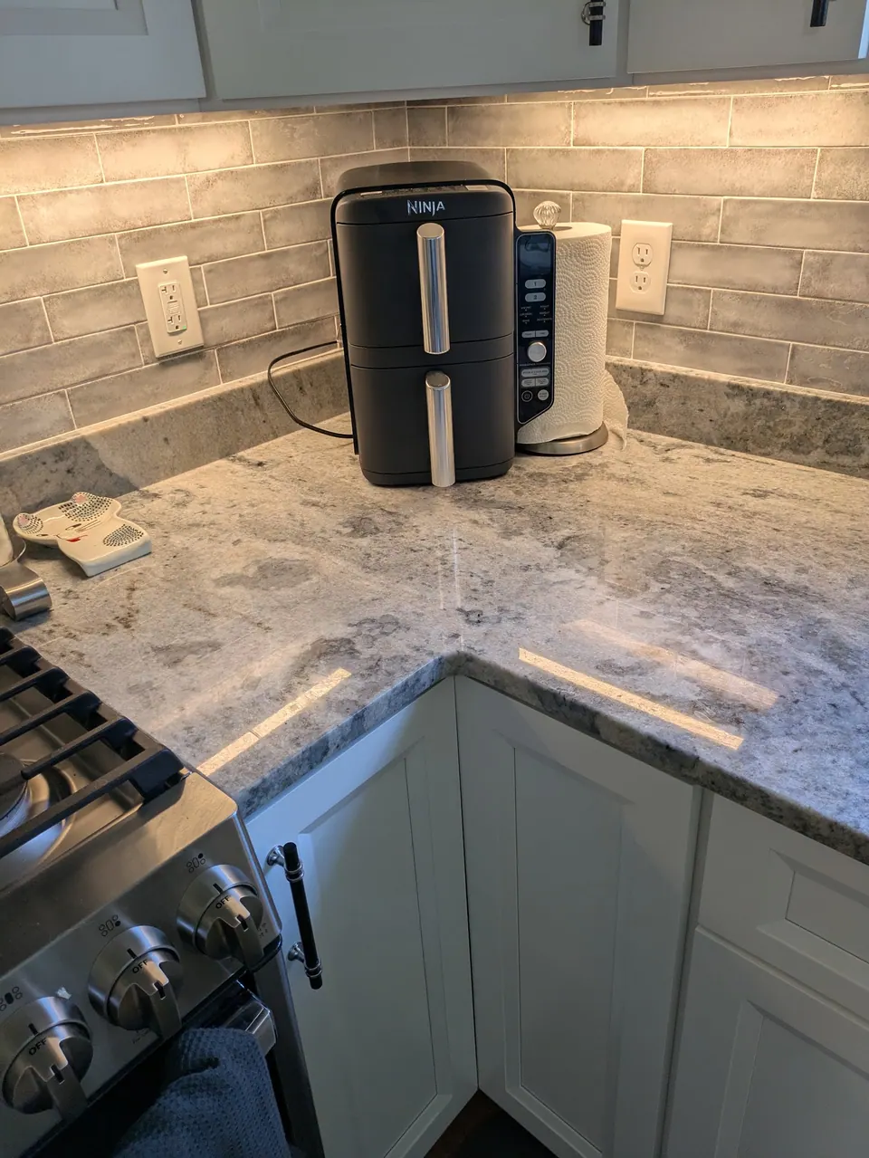 Light gray countertop corner with gray tile backsplash above white corner base doors.