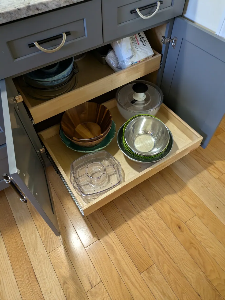 Gray base cabinet with doors open and a wood roll-out tray pulled out.