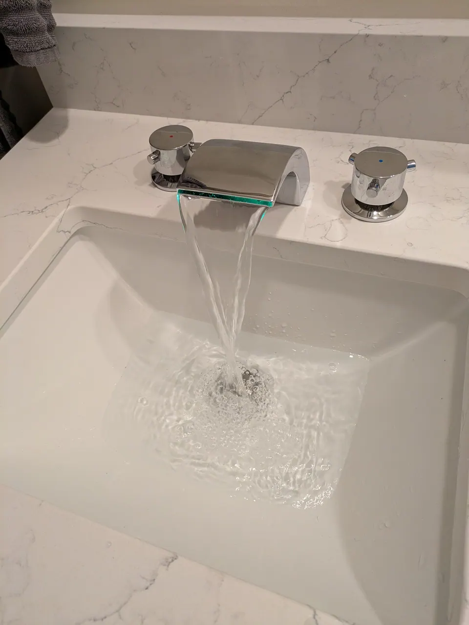 Bathroom: chrome waterfall faucet running into a white rectangular undermount sink.
