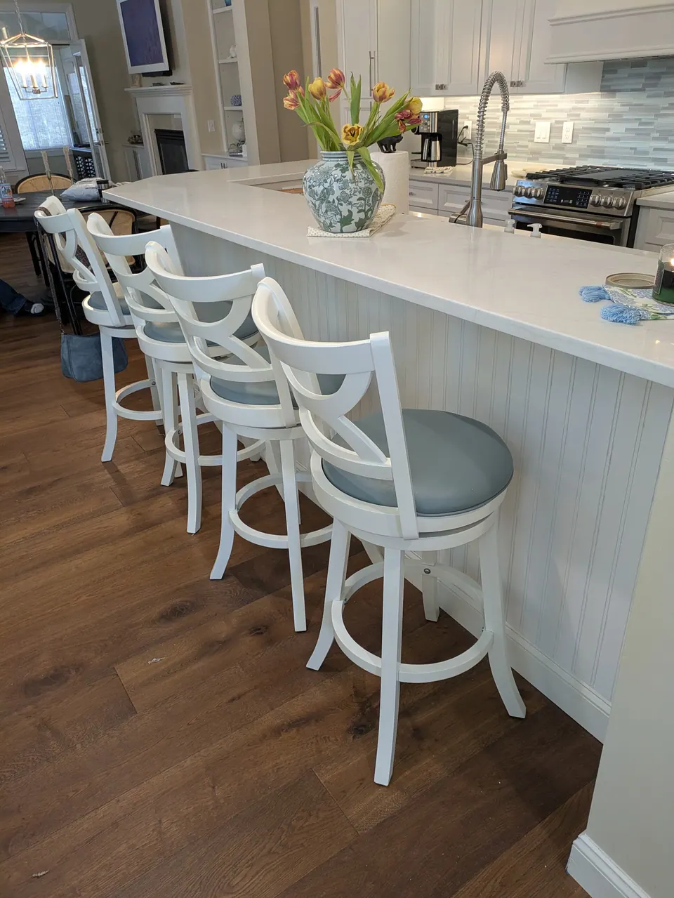 Island with a beadboard end and four white swivel bar stools with blue seats.