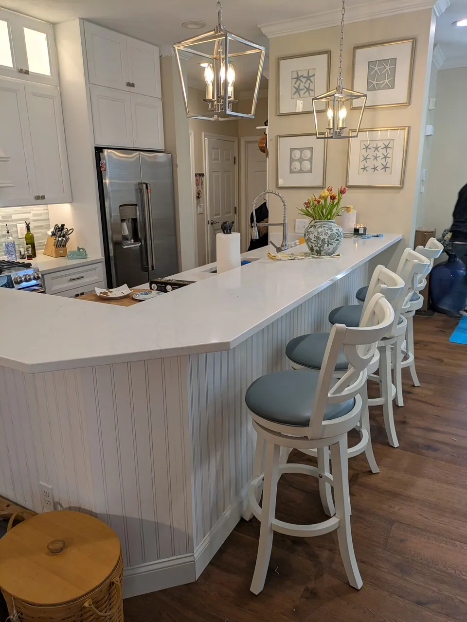 Long white island with bar stools seen from the dining area, the refrigerator and pantry cabinets behind.