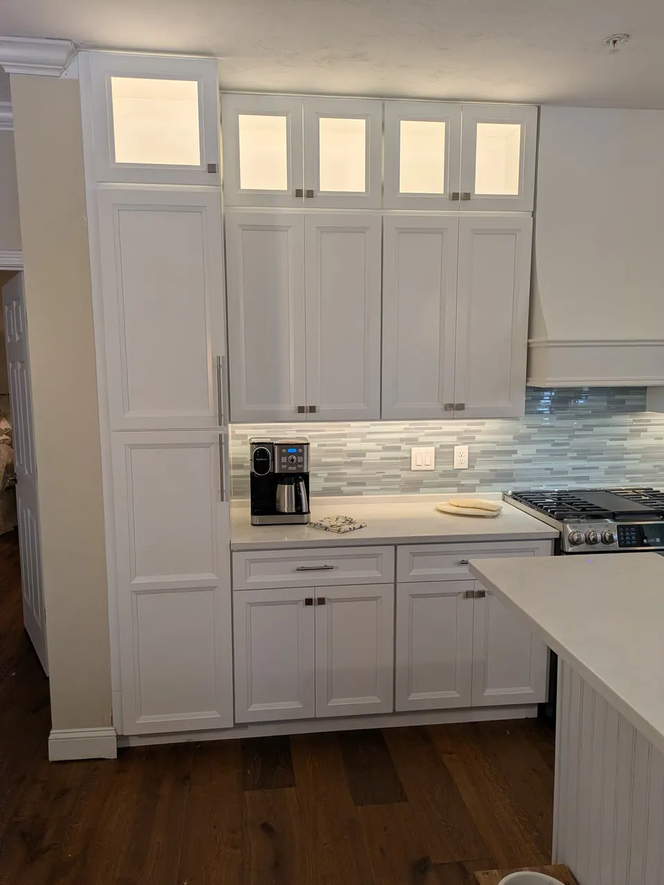 Tall white cabinets up to the ceiling with lit glass tops around the range hood.