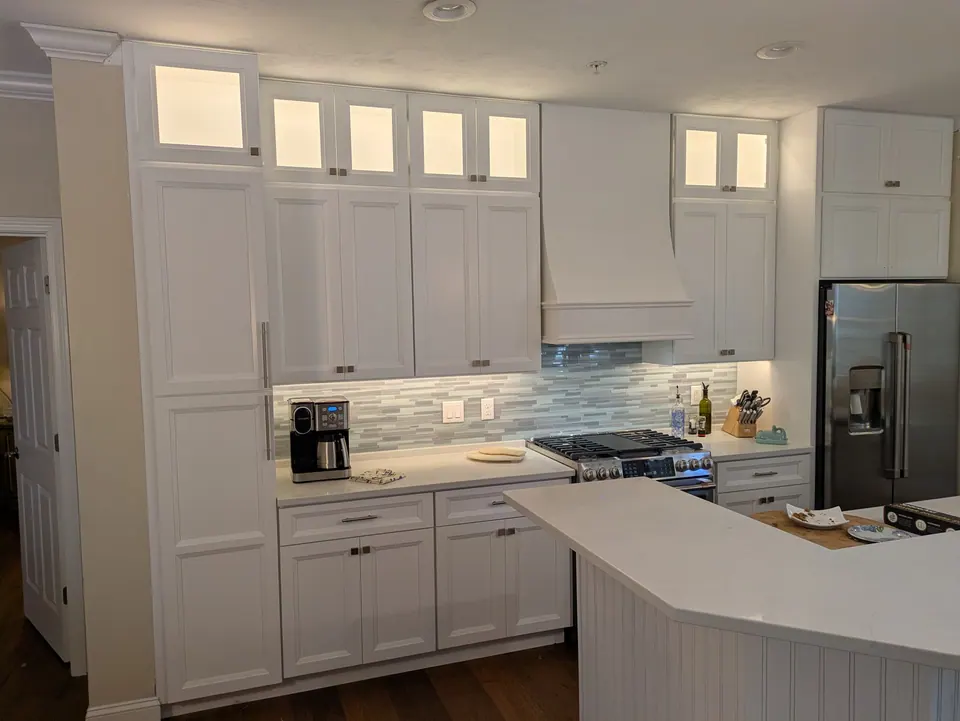The whole cooking wall: white cabinets to the ceiling, range hood and a stainless refrigerator.