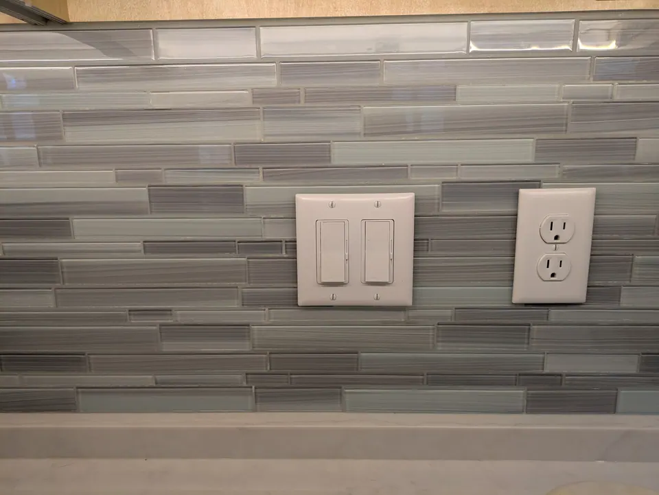 Gray and blue glass mosaic backsplash with outlets set into the tile.