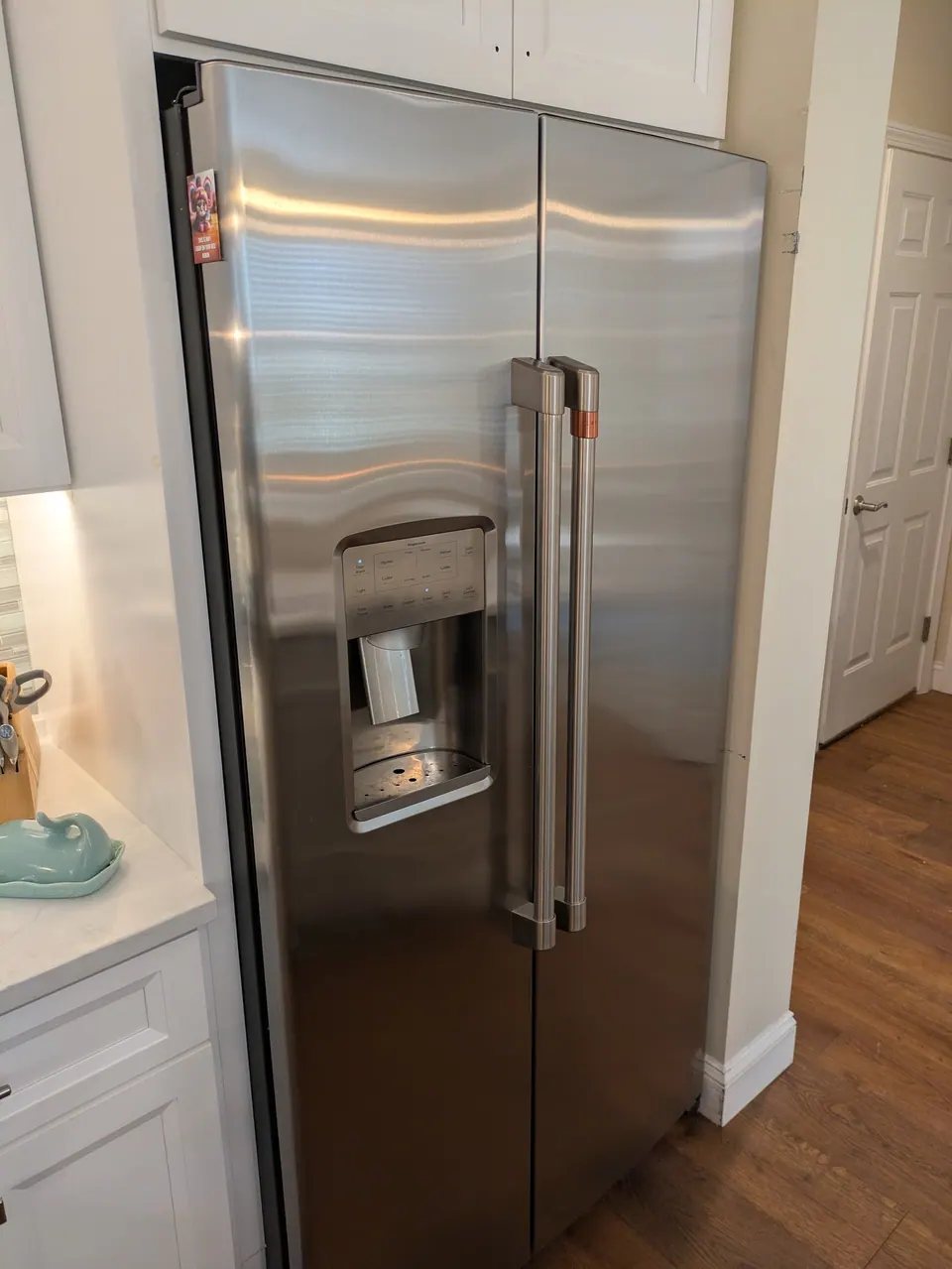 Stainless refrigerator framed by tall white cabinets.