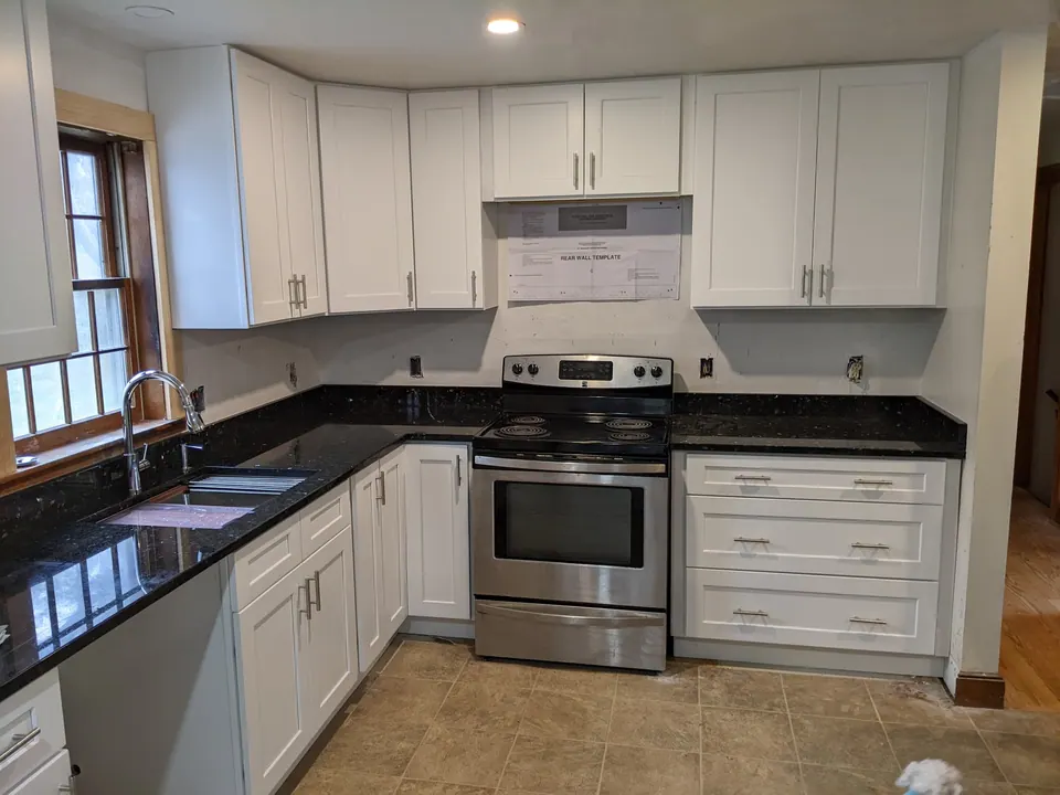 White shaker kitchen with black granite counters, a stainless range and microwave.