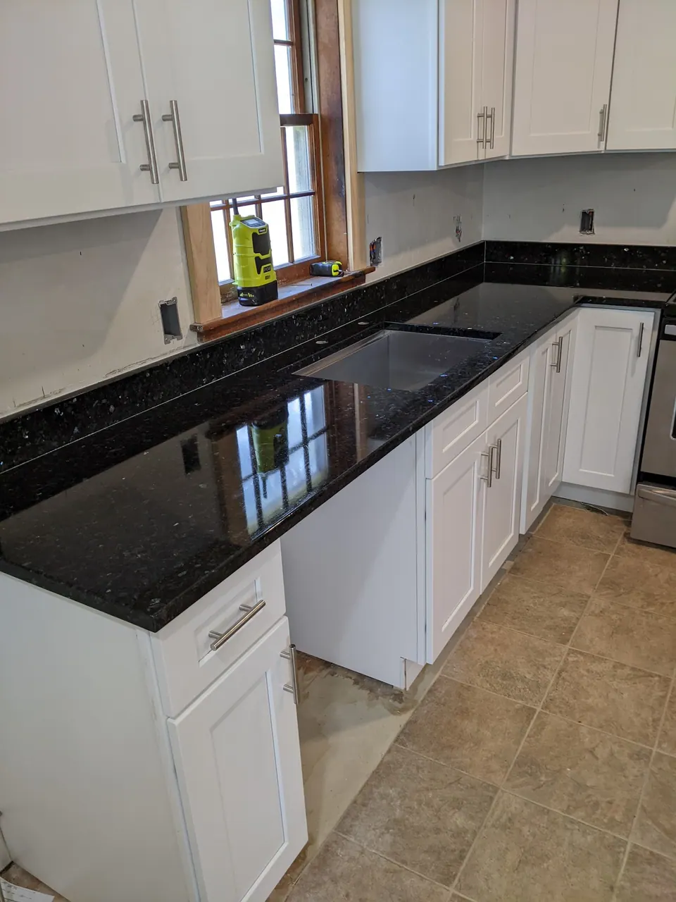 Sink run of white shaker cabinets with a black granite counter.