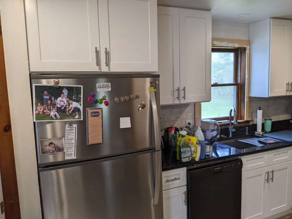White wall cabinets over the refrigerator and the sink window.