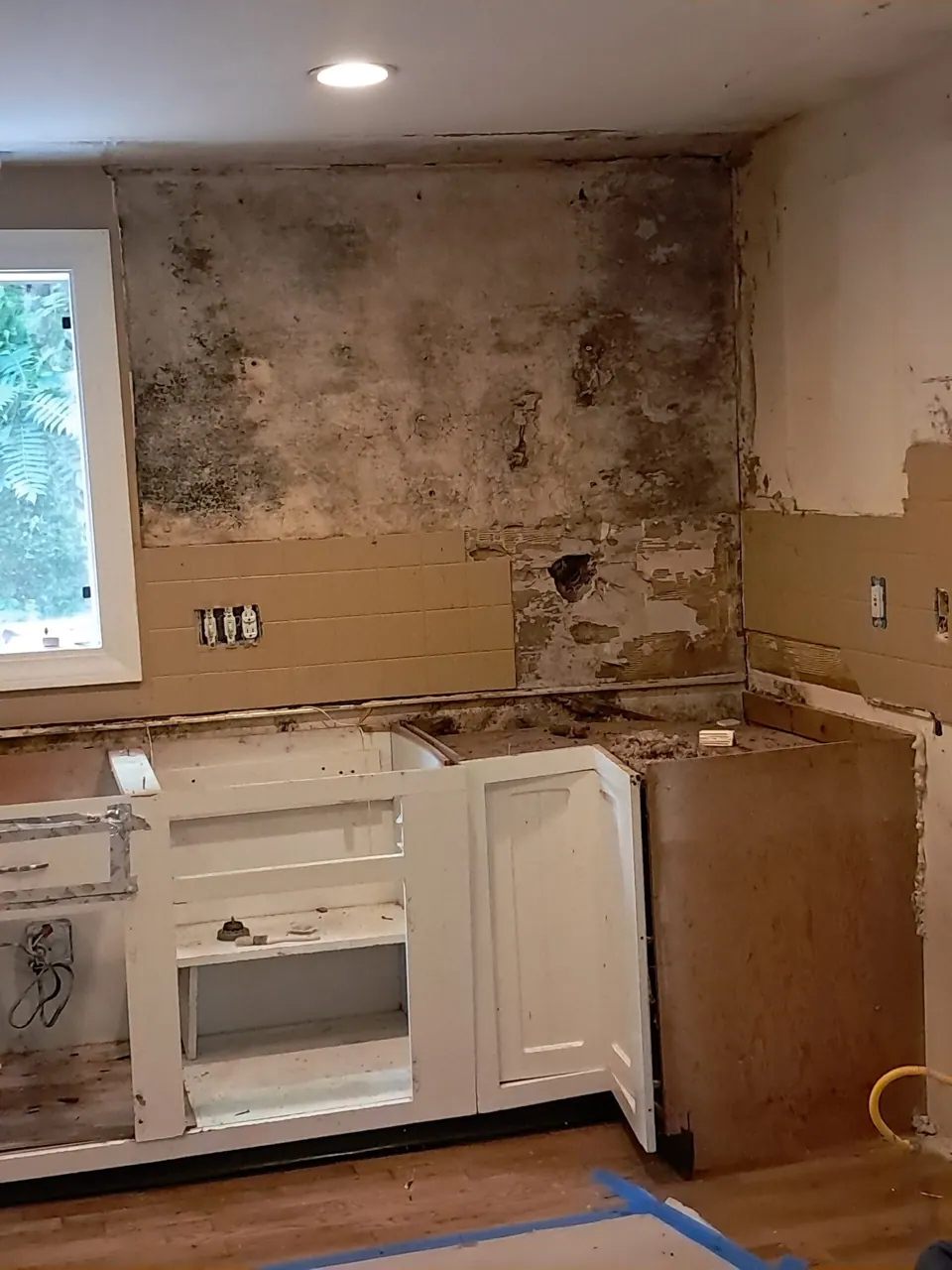 Demolition in progress: old white base cabinets without countertop below a bare, dark-stained wall.