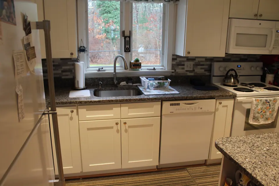 Sink run of white shaker cabinets under the window, gray granite counter.
