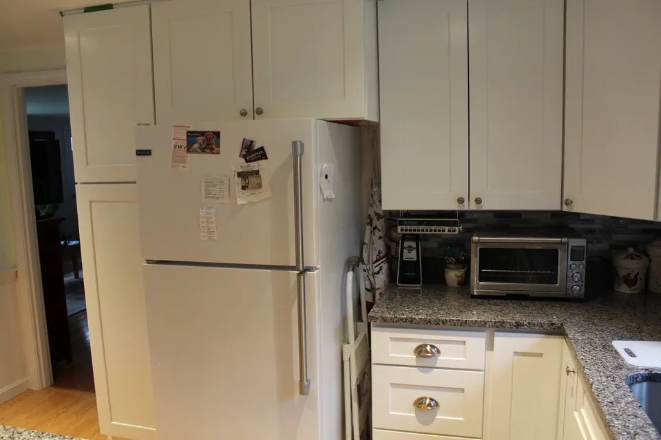 Refrigerator beside a tall white pantry cabinet.